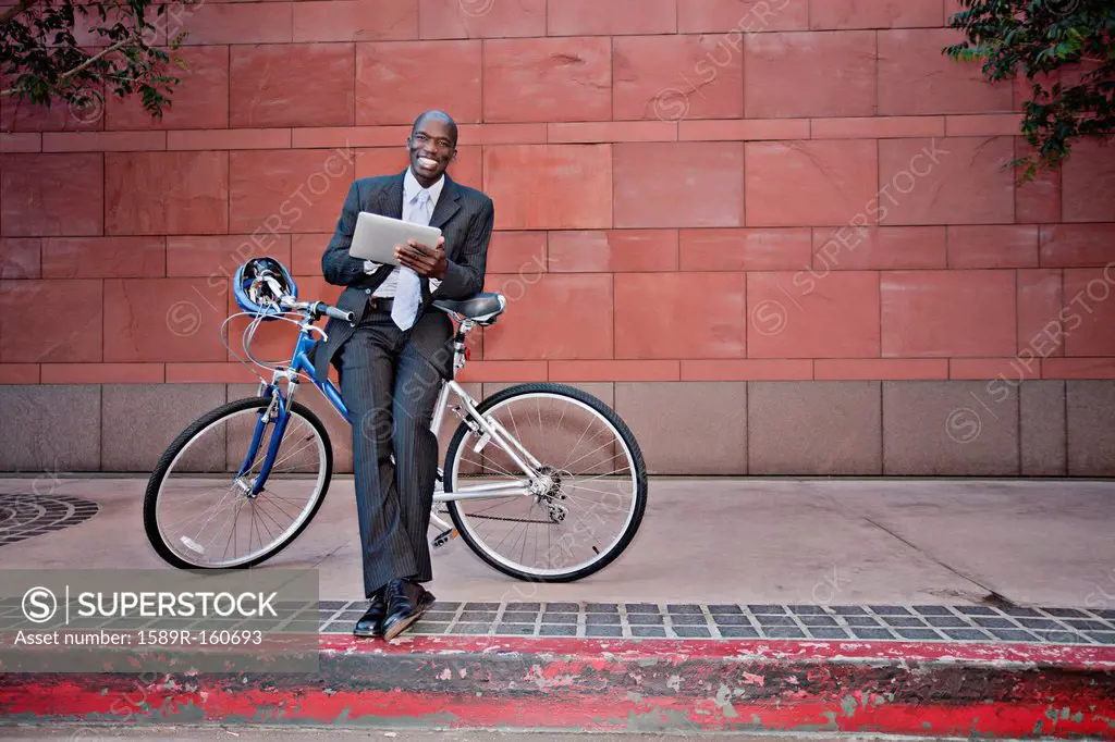 Businessman leaning on bicycle using digital tablet