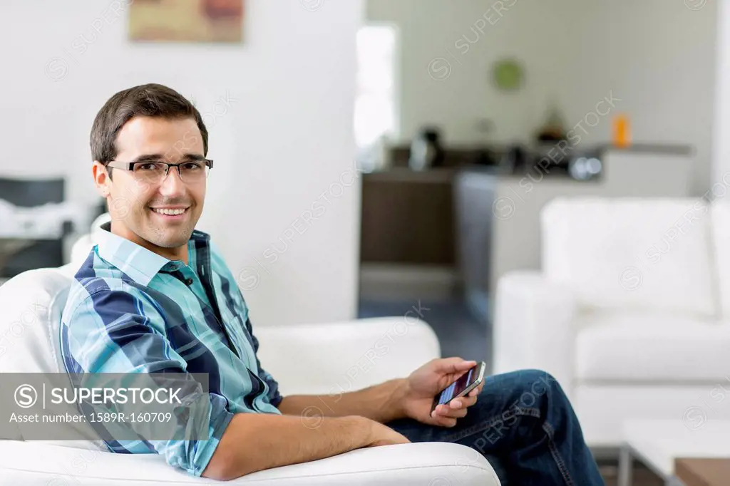 Mixed race man sitting on sofa holding cell phone