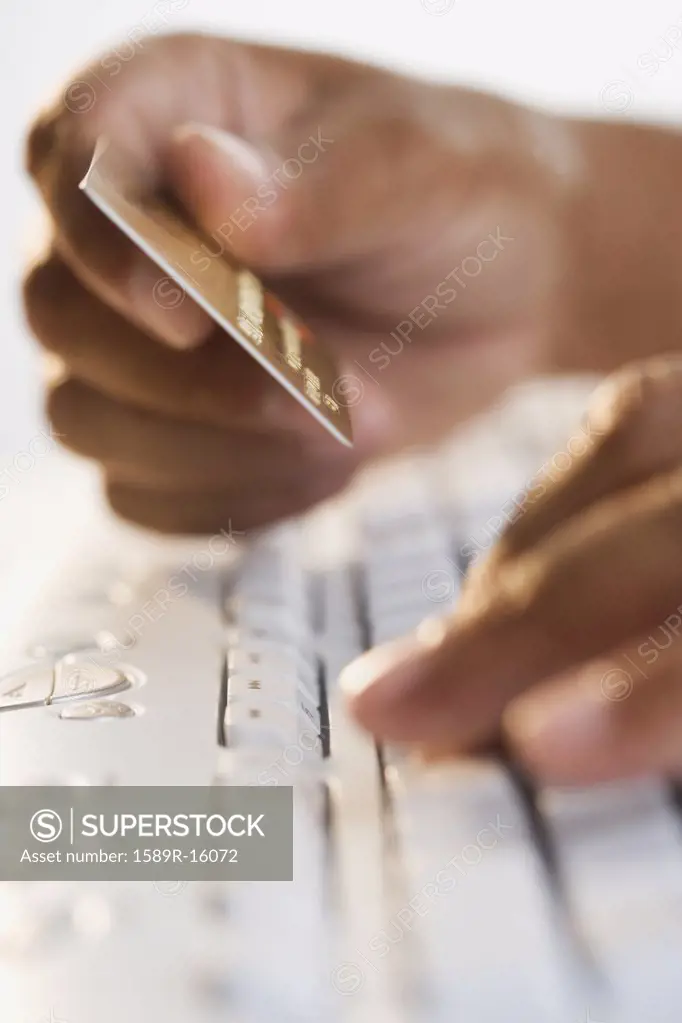 Close up of hands typing on keyboard and holding credit card