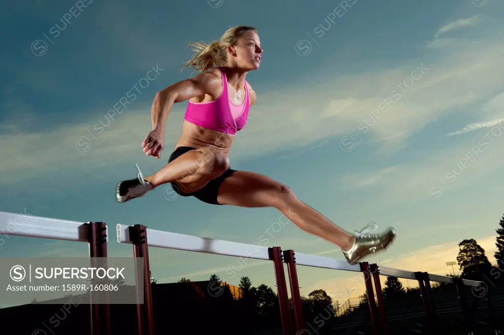 Caucasian runner jumping over hurdles