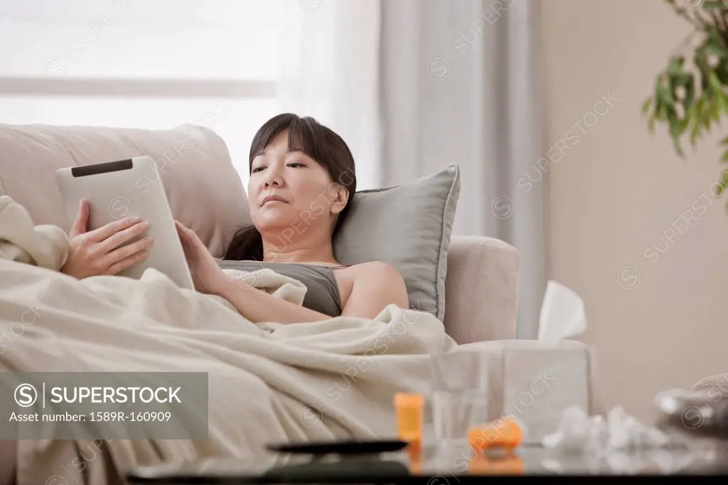 Sick Asian woman using digital tablet on sofa