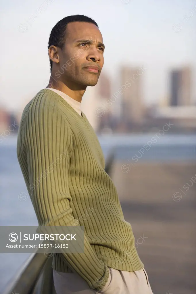 Man thinking while leaning against bridge with city behind him