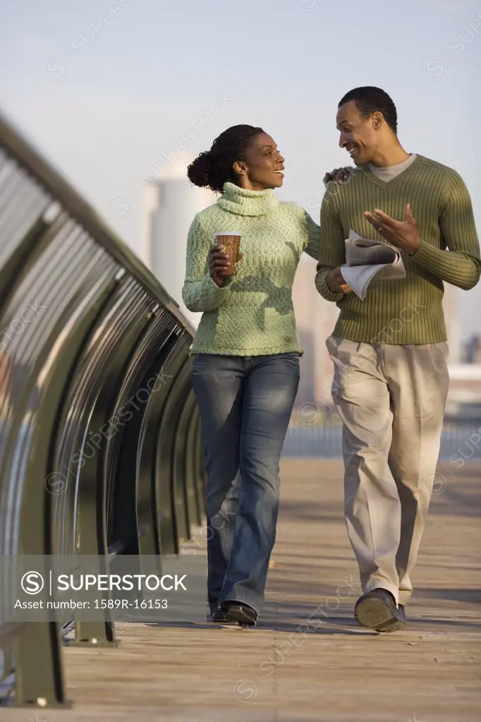 Couple walking across bridge with city behind them