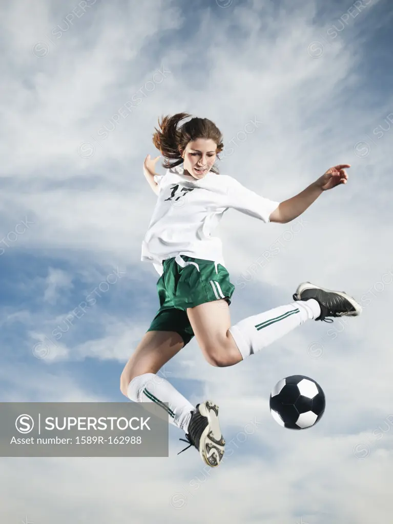 Caucasian teenager kicking soccer ball in mid_air