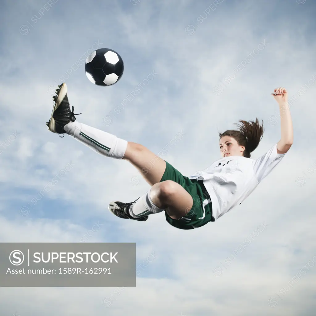 Caucasian teenager kicking soccer ball in mid_air