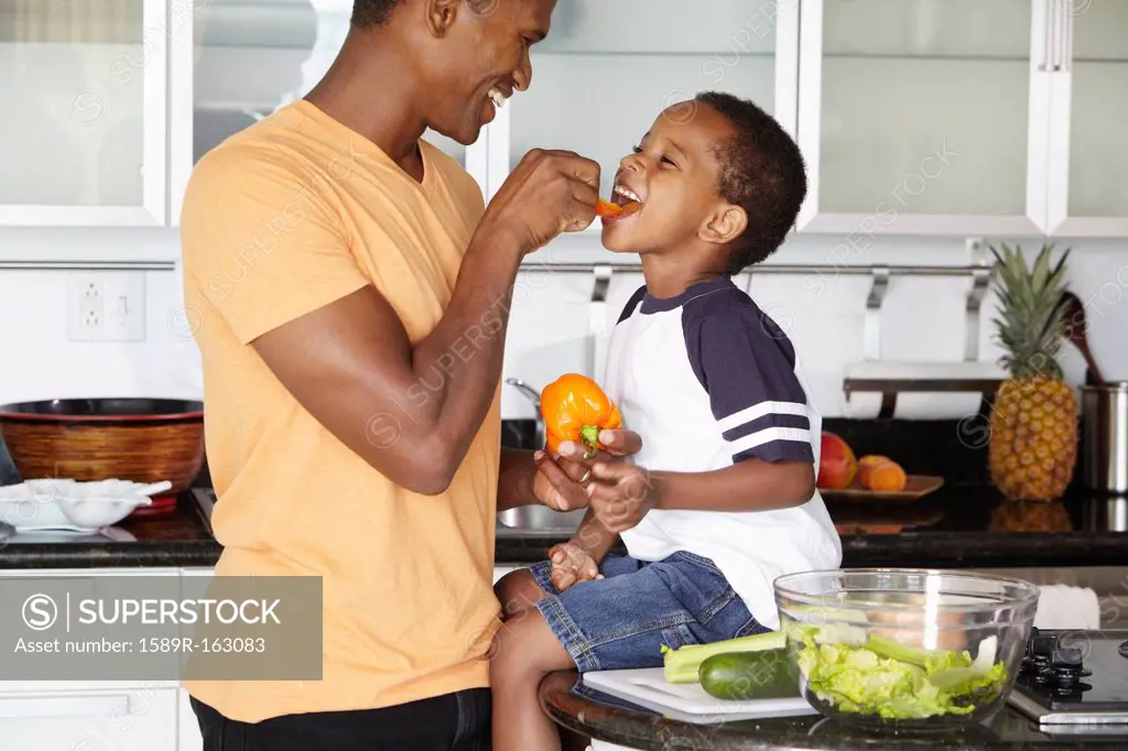 African American father and son eating vegetables in kitchen