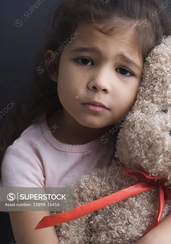 Portrait of girl crying and hugging teddy bear