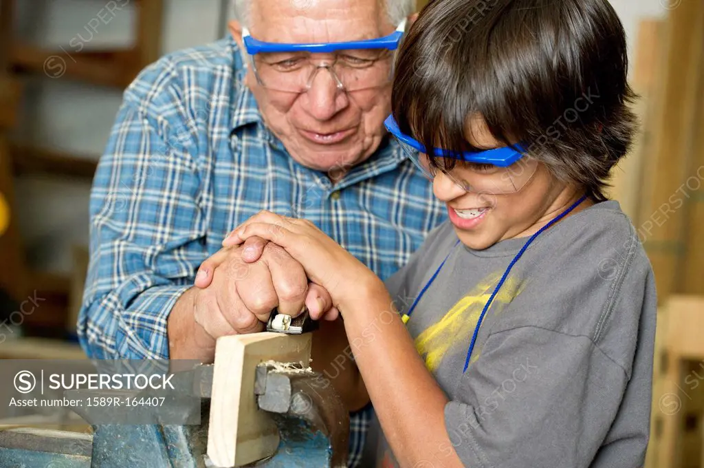 Hispanic grandfather and son planing wood in workshop