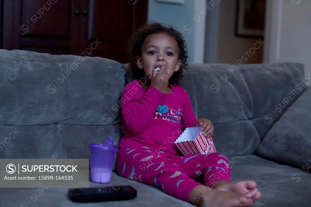 Mixed race girl eating popcorn and watching television