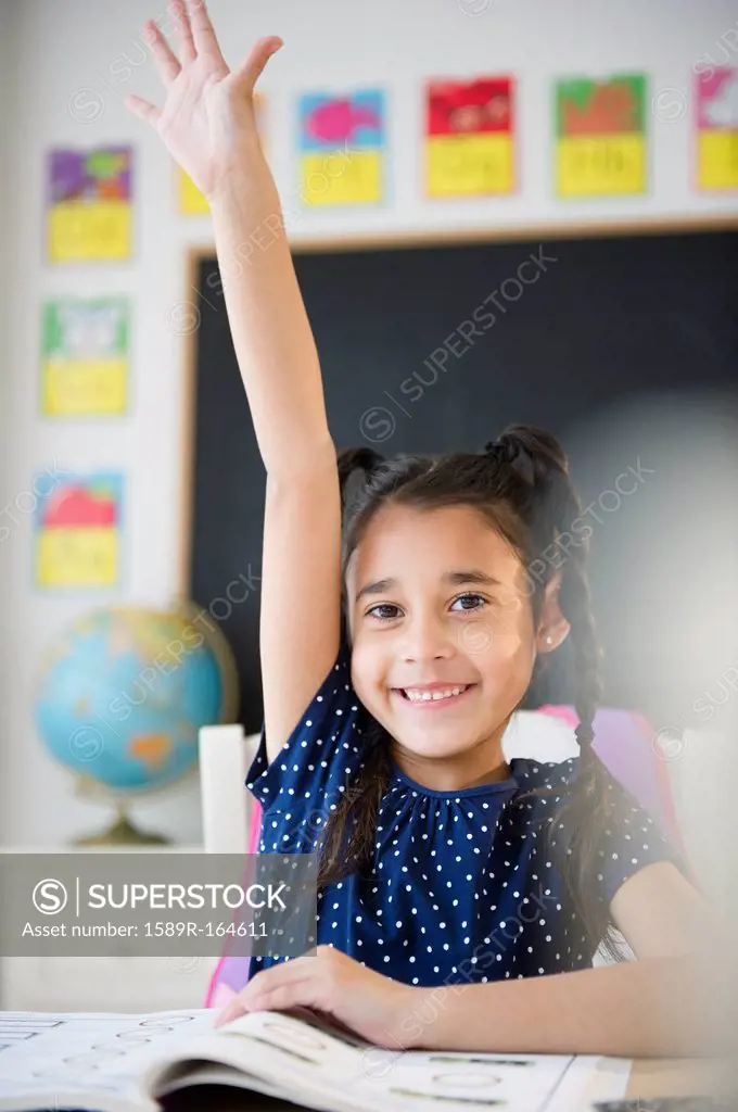 Mixed race girl raising her hand in classroom