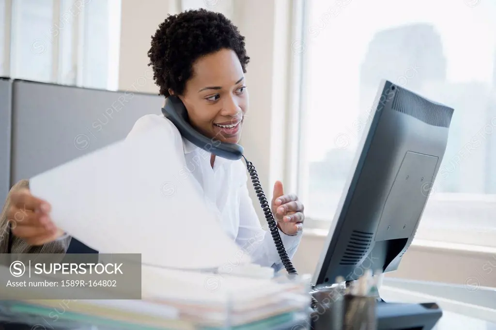 African American businesswoman using computer and talking on telephone