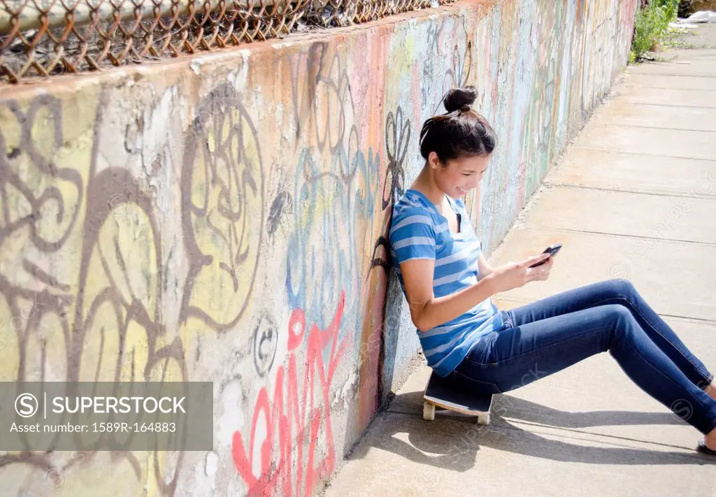 Asian woman sitting on skateboard using cell phone
