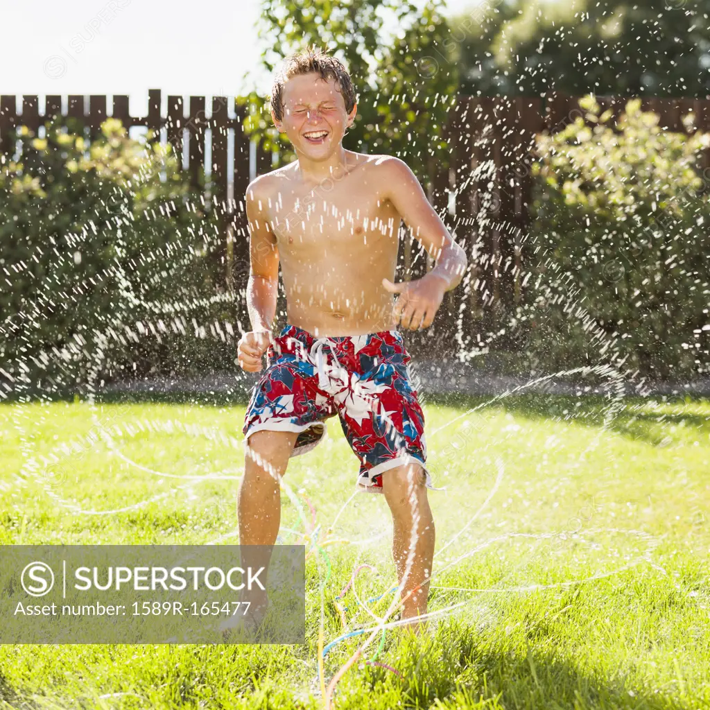Caucasian boy playing in sprinkler