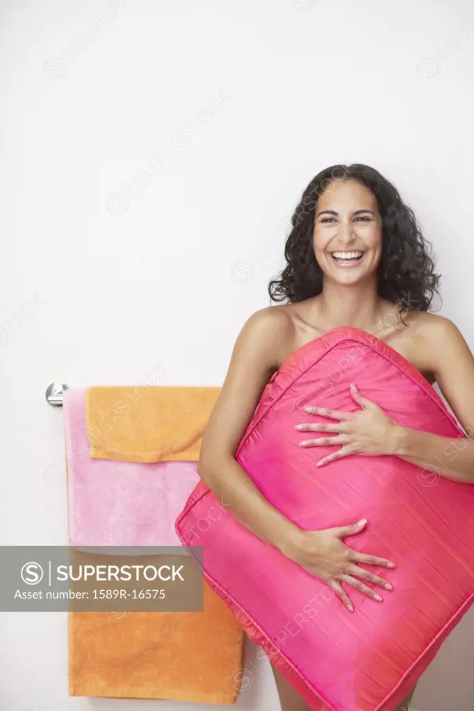Young woman holding a large pillow over her naked body
