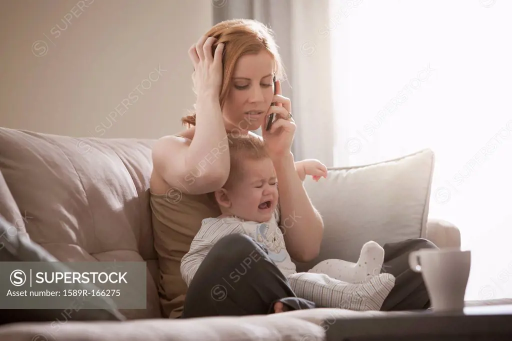 Caucasian mother holding crying son and talking on cell phone