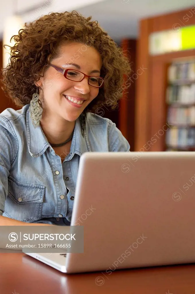 Hispanic woman using laptop in library