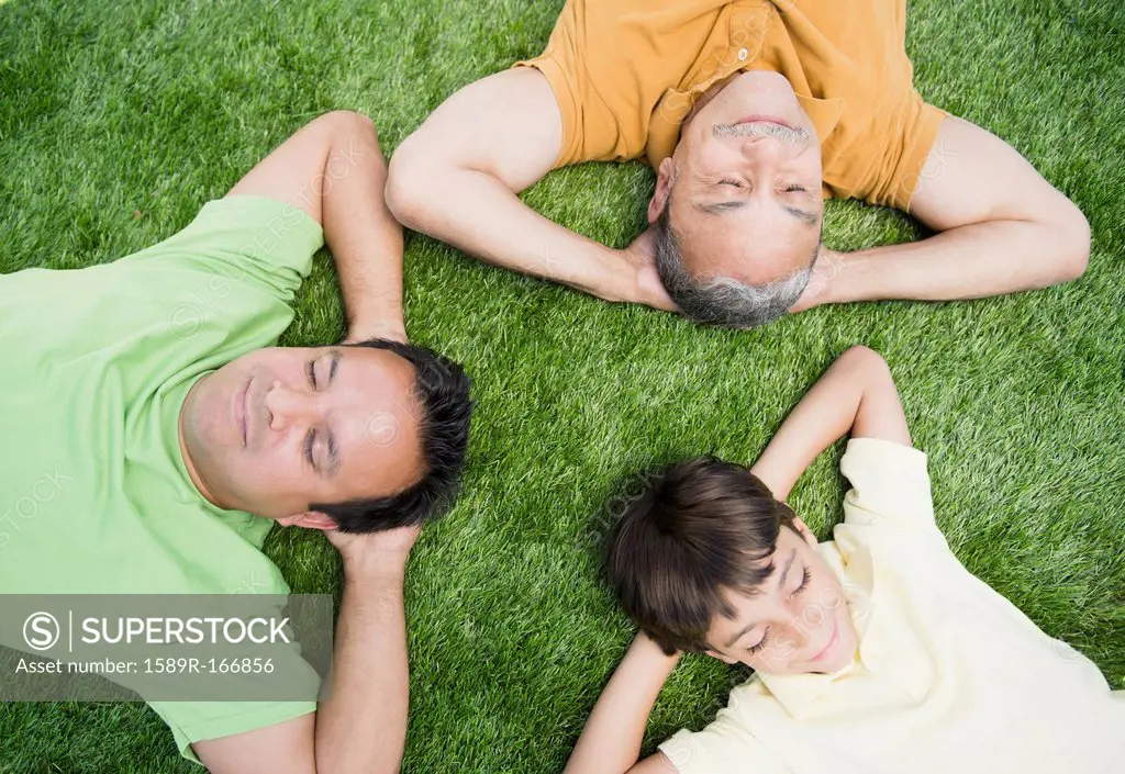 Hispanic grandfather, father and son laying in grass
