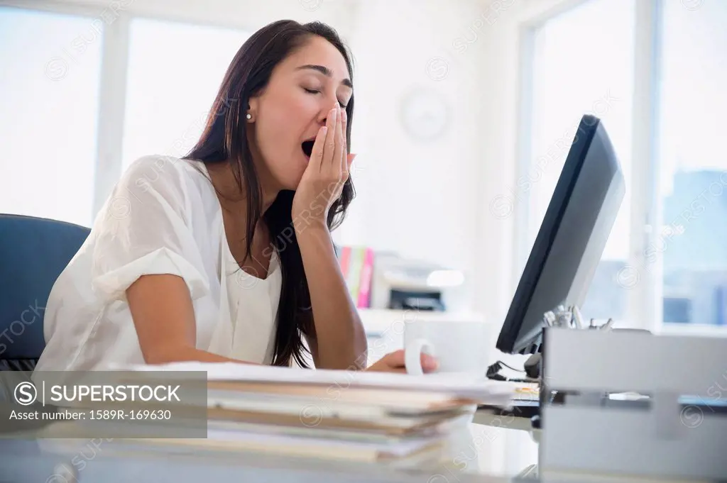 Caucasian businesswoman yawning at desk