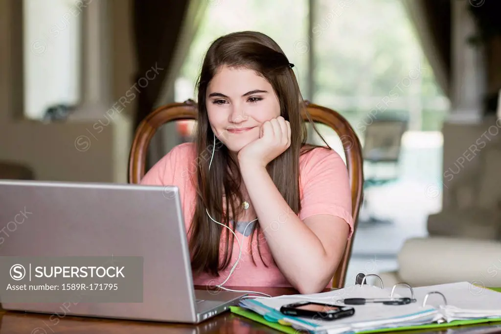 Caucasian girl using laptop and listening to mp3 player