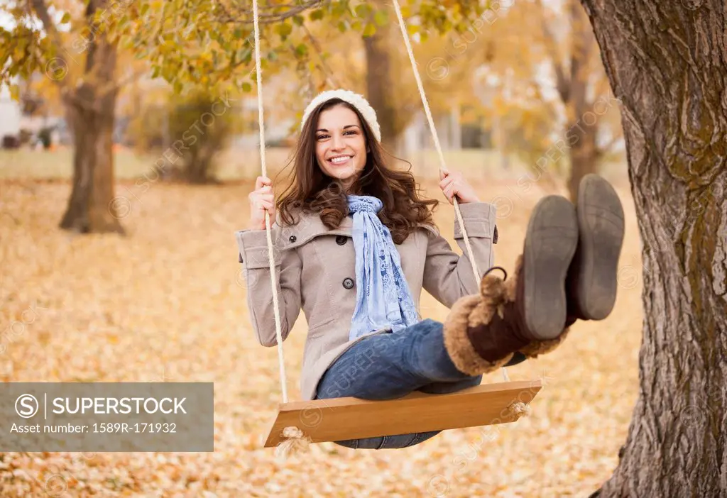 Caucasian woman sitting on swing in autumn leaves