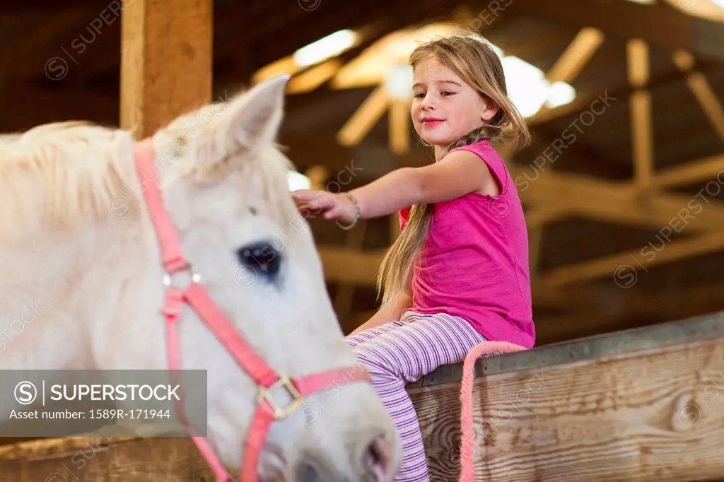 Caucasian girl petting horse in barn