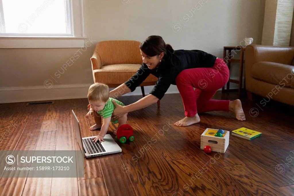 Caucasian mother keeping toddler son from laptop