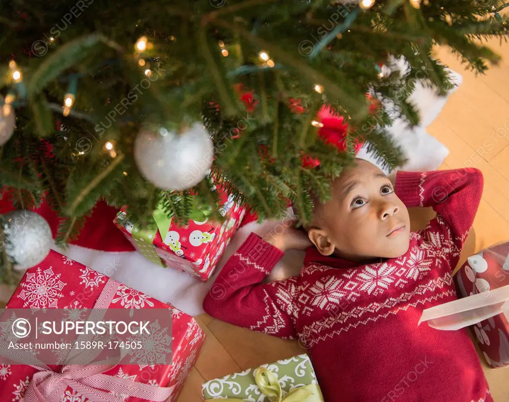 African American boy laying under Christmas tree