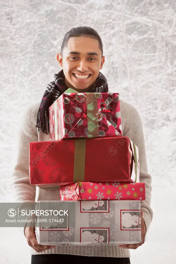 Hispanic man holding stack of presents in snow