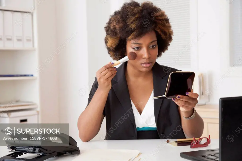 African American businesswoman applying makeup in office