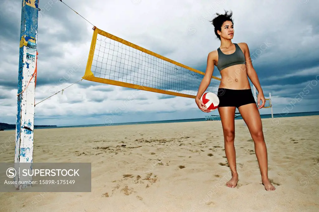 Mixed race woman holding volleyball on beach
