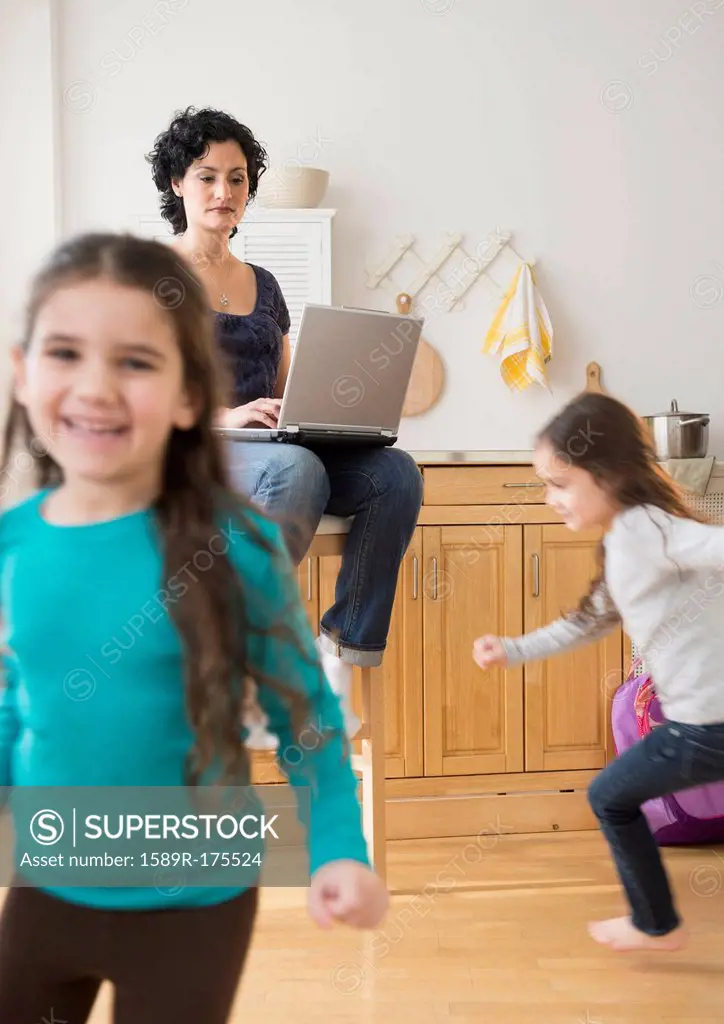 Mother using laptop as daughters play