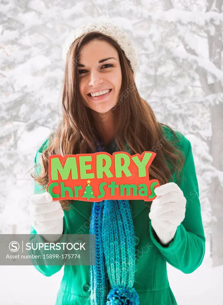 Caucasian woman holding 'Merry Christmas' sign in snow