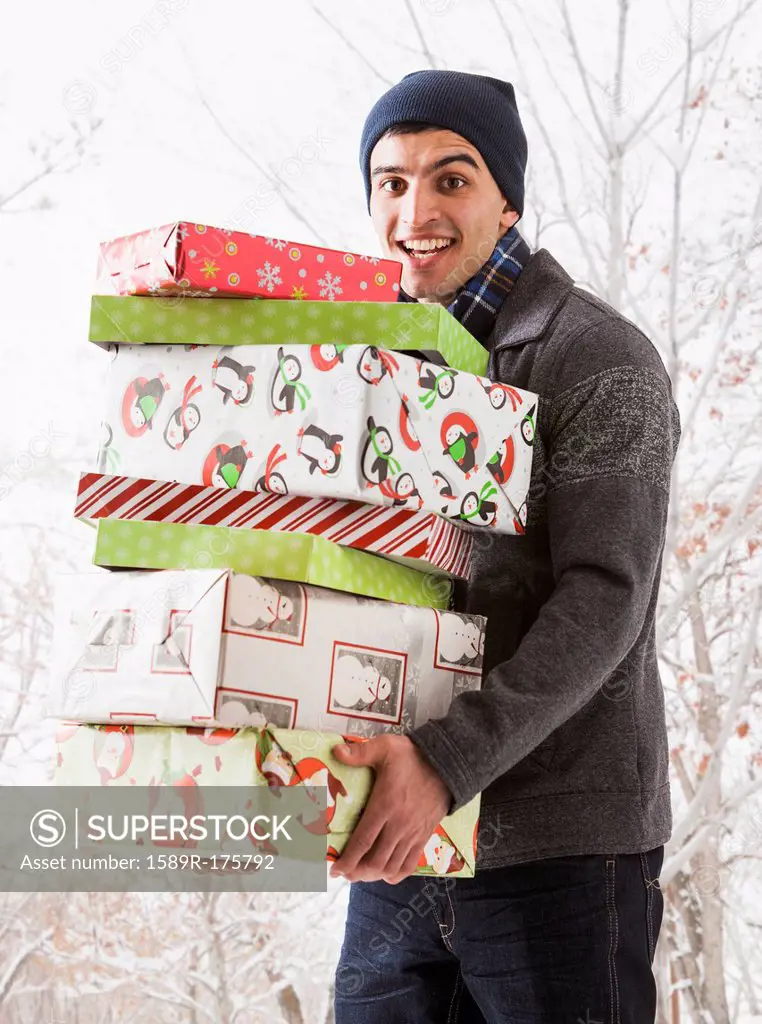 Hispanic man holding Christmas gifts in snow
