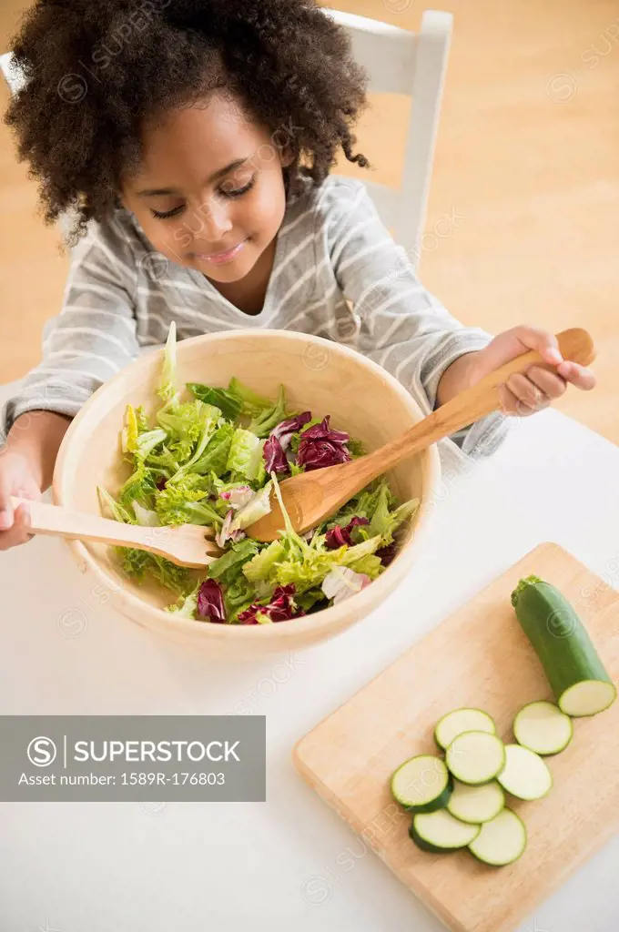 African American girl tossing salad at table