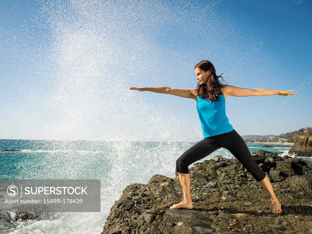 Mixed race woman practicing yoga on rocky beach