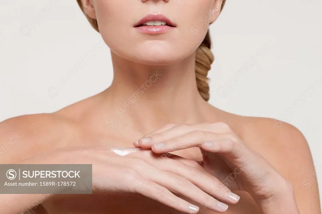 Nude Caucasian woman applying moisturizer