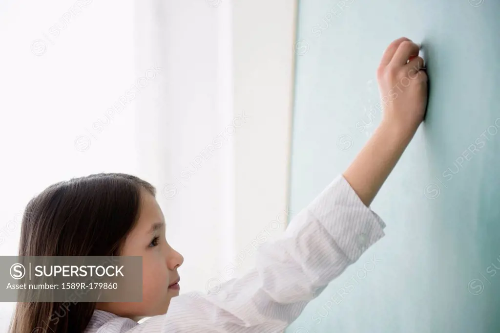 Mixed race girl writing on chalkboard