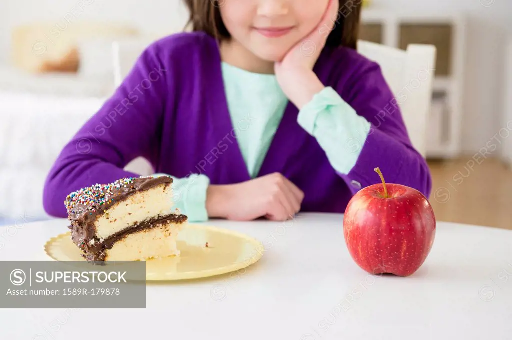 Mixed race girl choosing between cake and apple