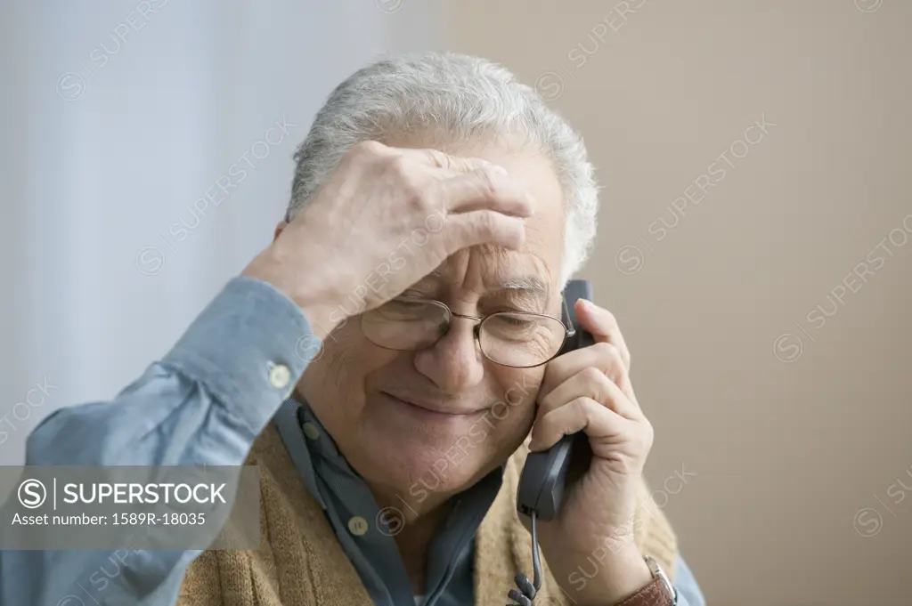 Older man rubbing his forehead as he talks on the telephone