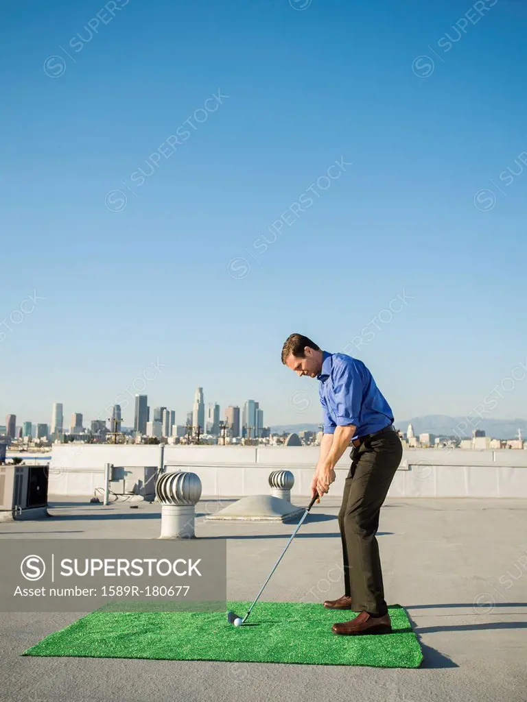 Caucasian businessman playing golf on urban rooftop