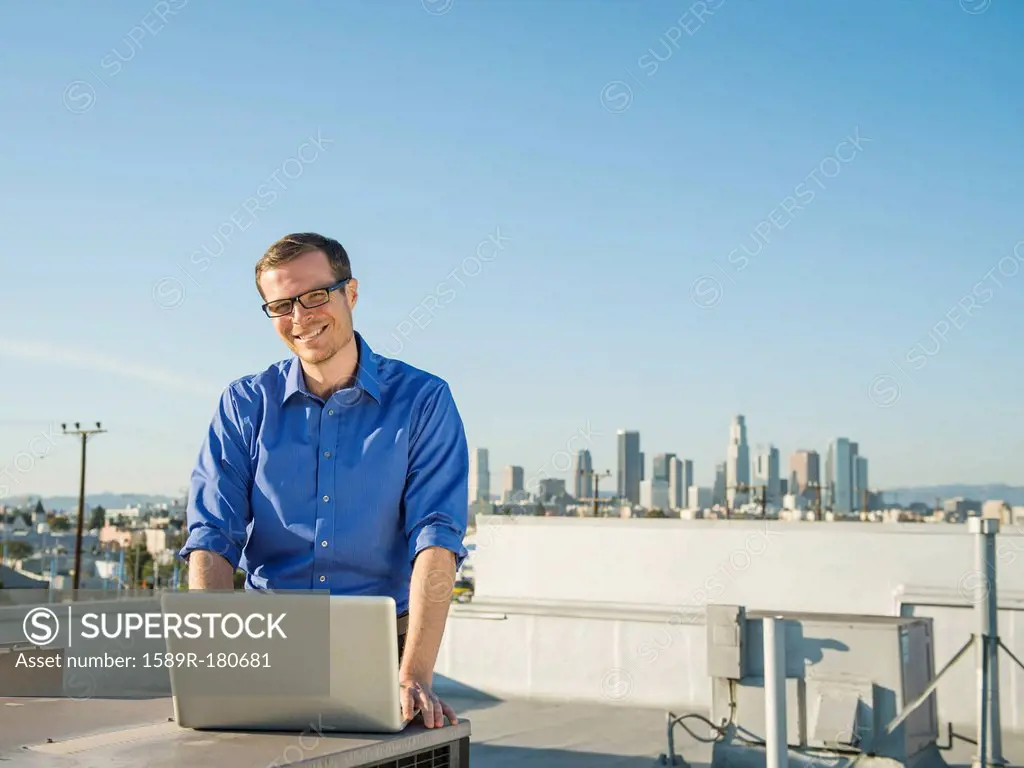Caucasian businessman using laptop on urban rooftop