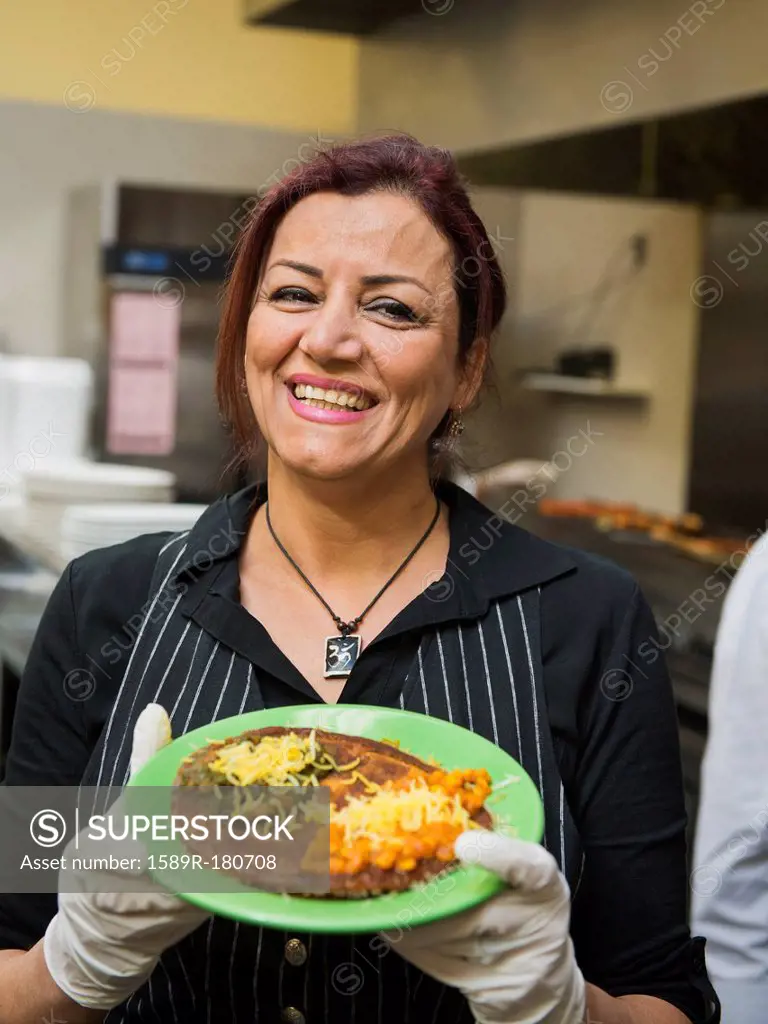 Mixed race chef holding plate of food in kitchen