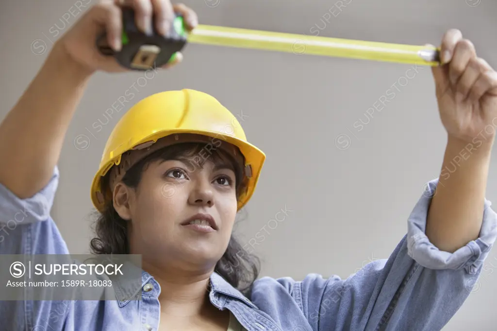 Woman construction worker with measuring tape and hard hat