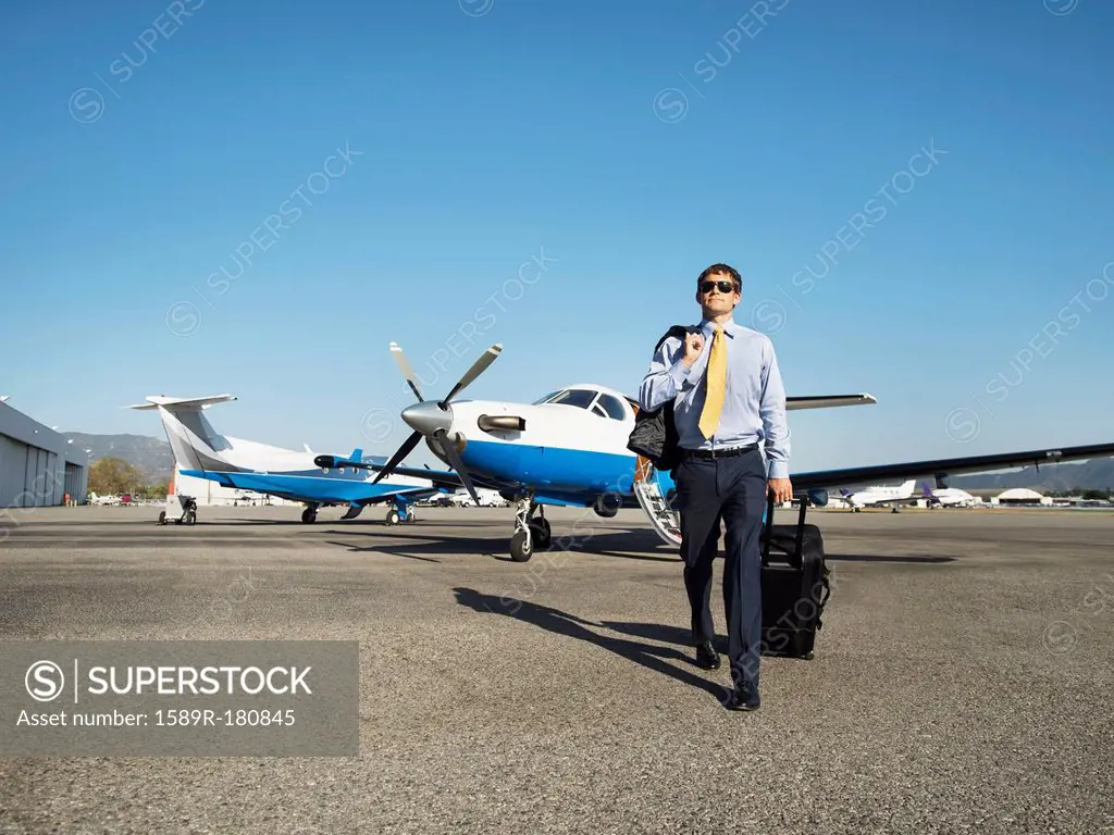 Caucasian businessman rolling luggage on runway