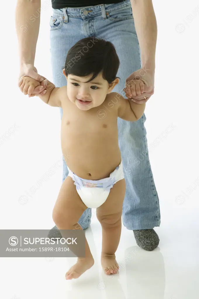 Toddler boy in diaper walking with help of parent