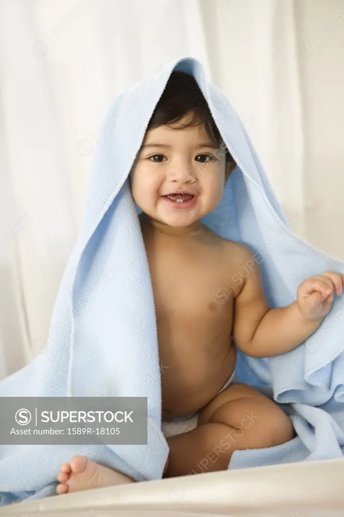 Toddler boy in diaper smiling with blanket over his head