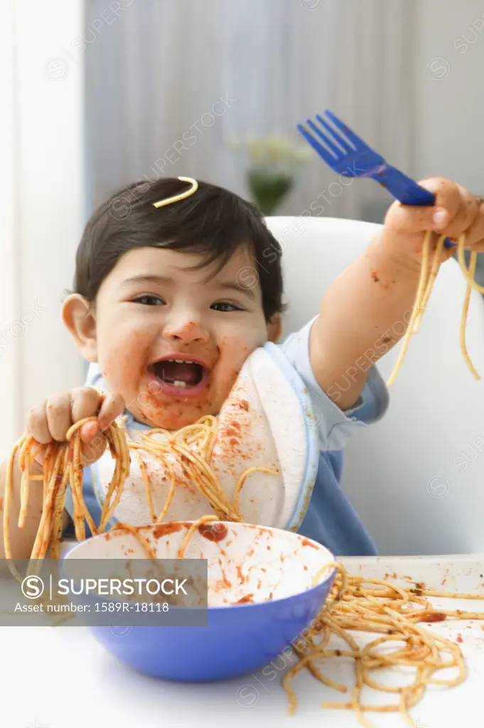 Baby boy in high chair laughing spaghetti mess