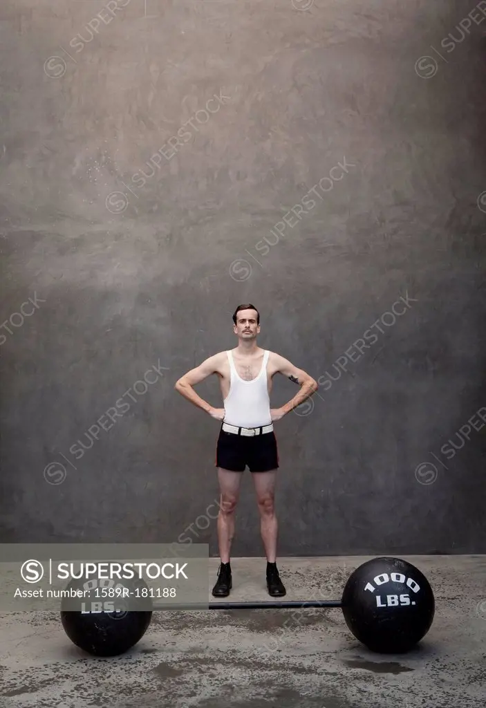 Skinny Caucasian weight lifter standing by weights