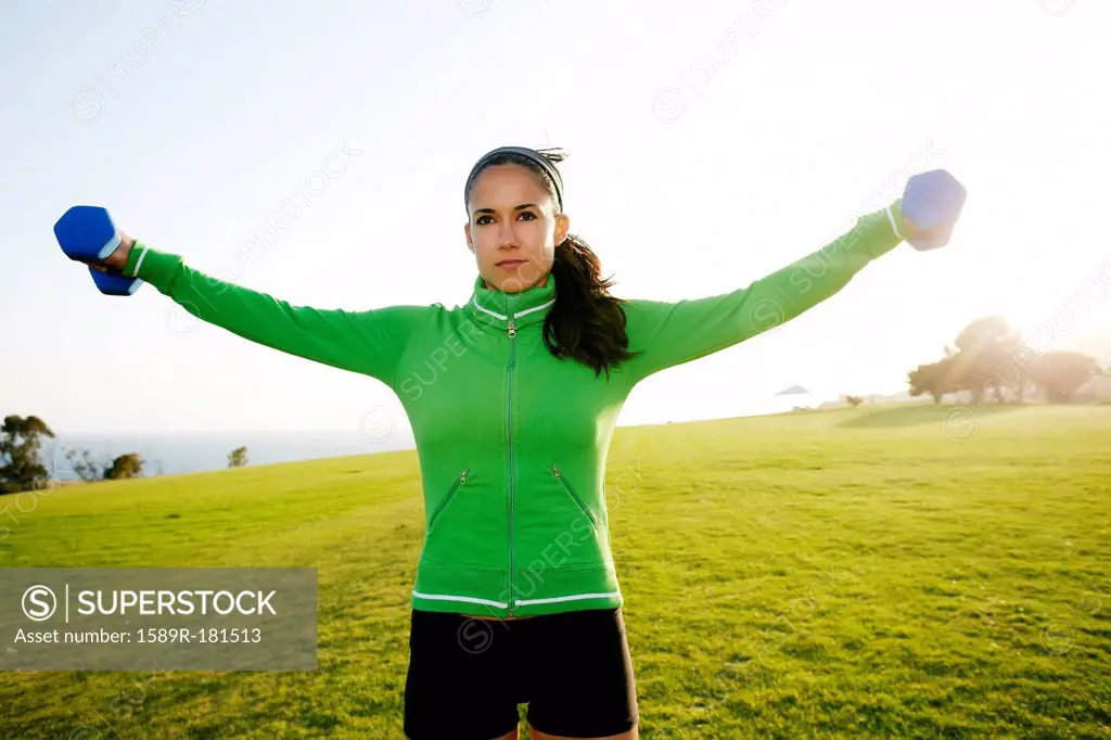 Hispanic woman lifting weights in field