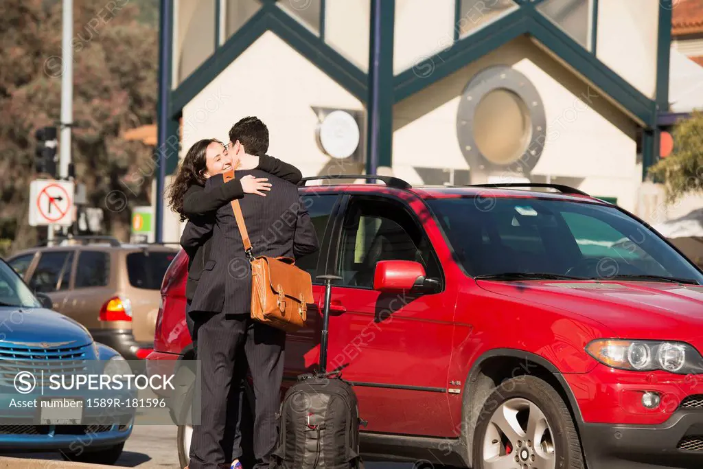Hispanic couple hugging in parking lot